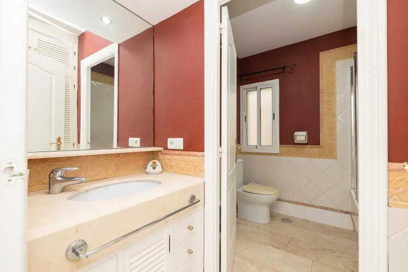 A bathroom with a sink vanity in the foreground and a toilet beyond.