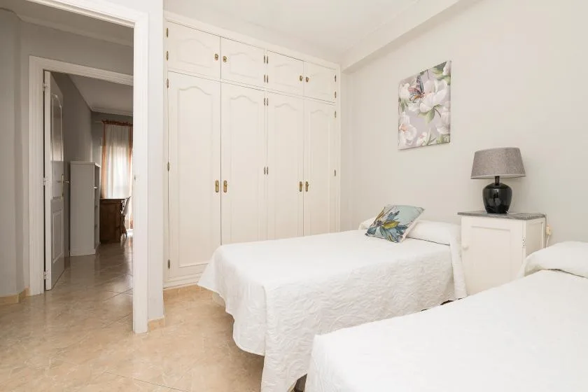 A bright bedroom with two beds, built-in wardrobes, and a bedside table.