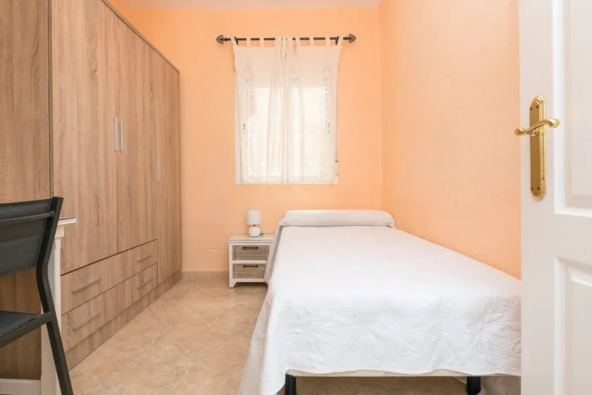 A bedroom with a bed, a wooden wardrobe, and a curtained window.