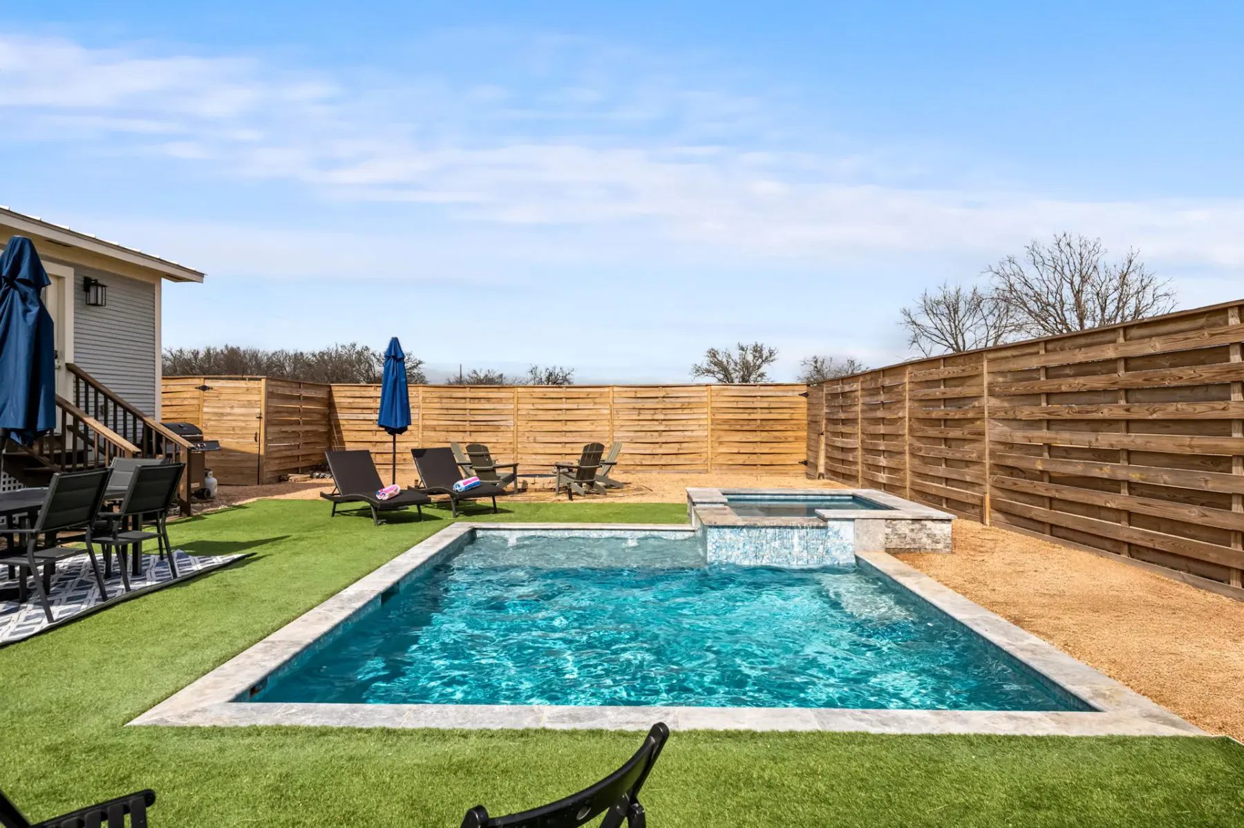 A backyard swimming pool sits beside a smaller raised pool and fenced patio.