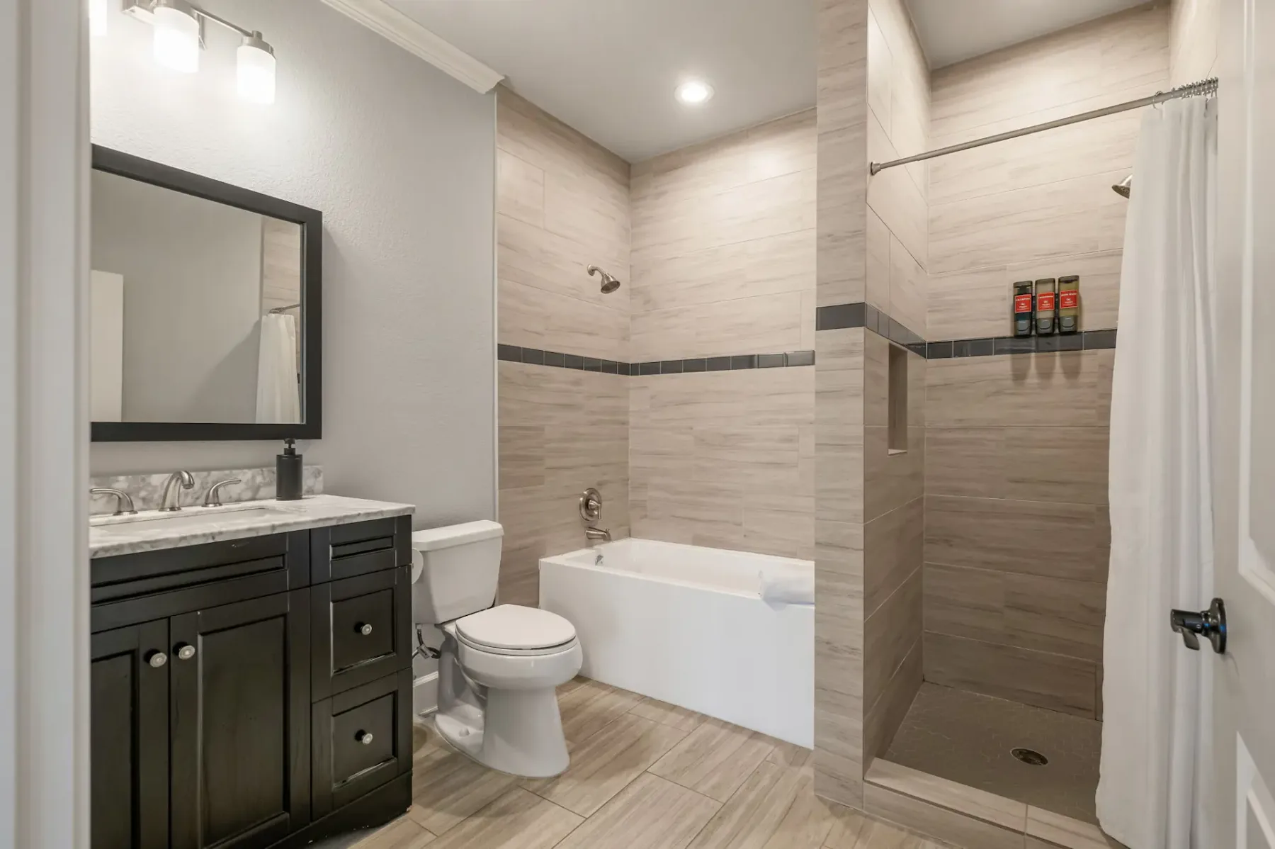 A bathroom with a dark vanity, toilet, bathtub, and shower.