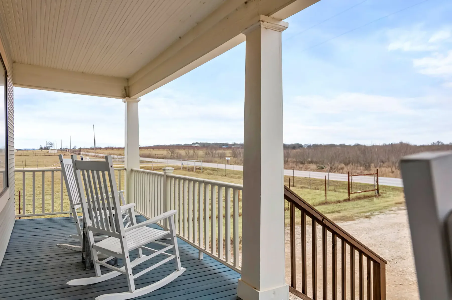 A covered porch with rocking chairs overlooks an open field.
