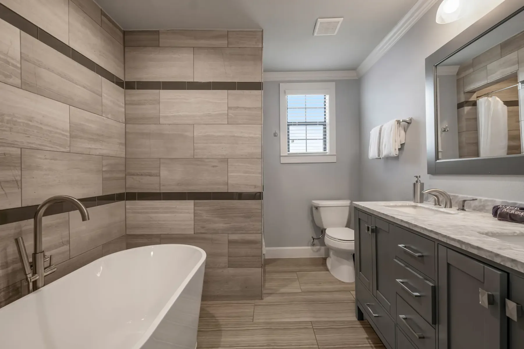 A bathroom with a bathtub, tiled walls, a vanity, and a window.