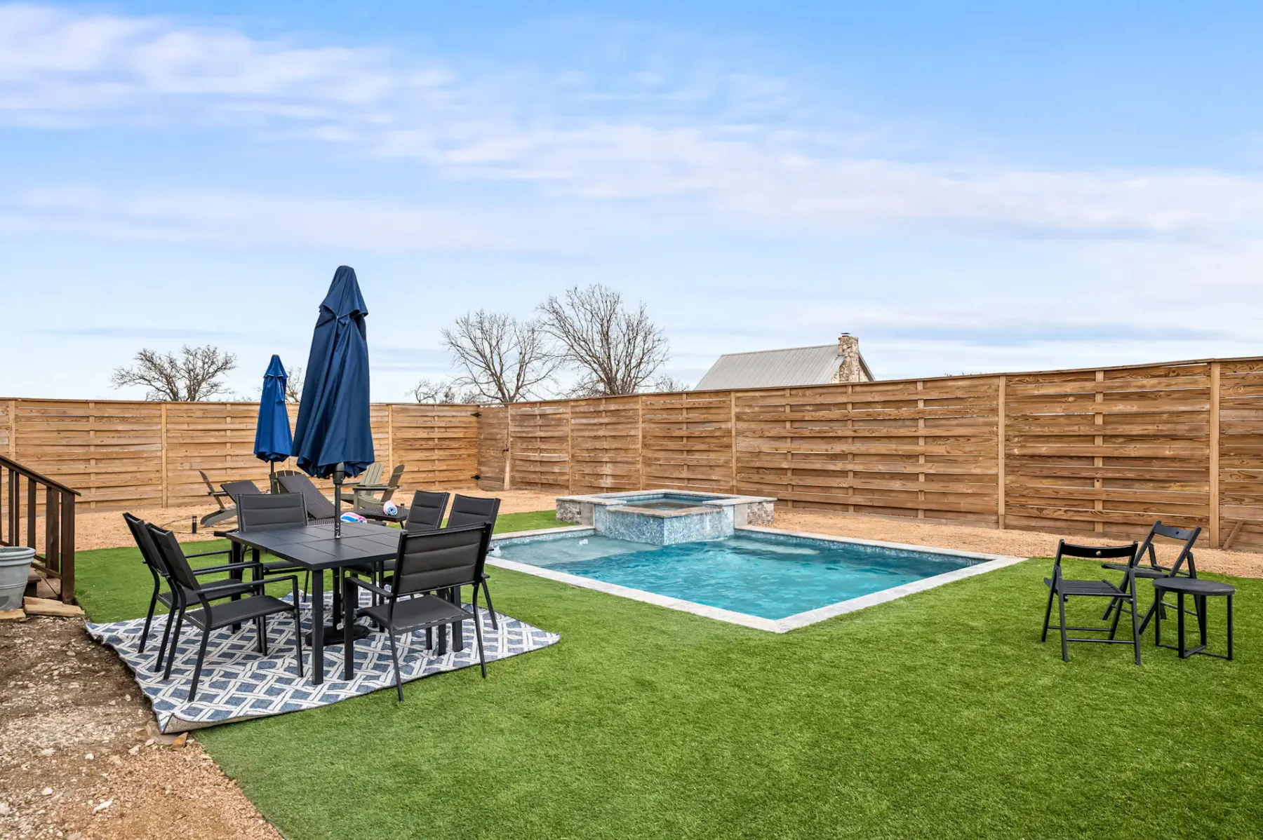 A fenced backyard patio with outdoor seating beside a swimming pool.