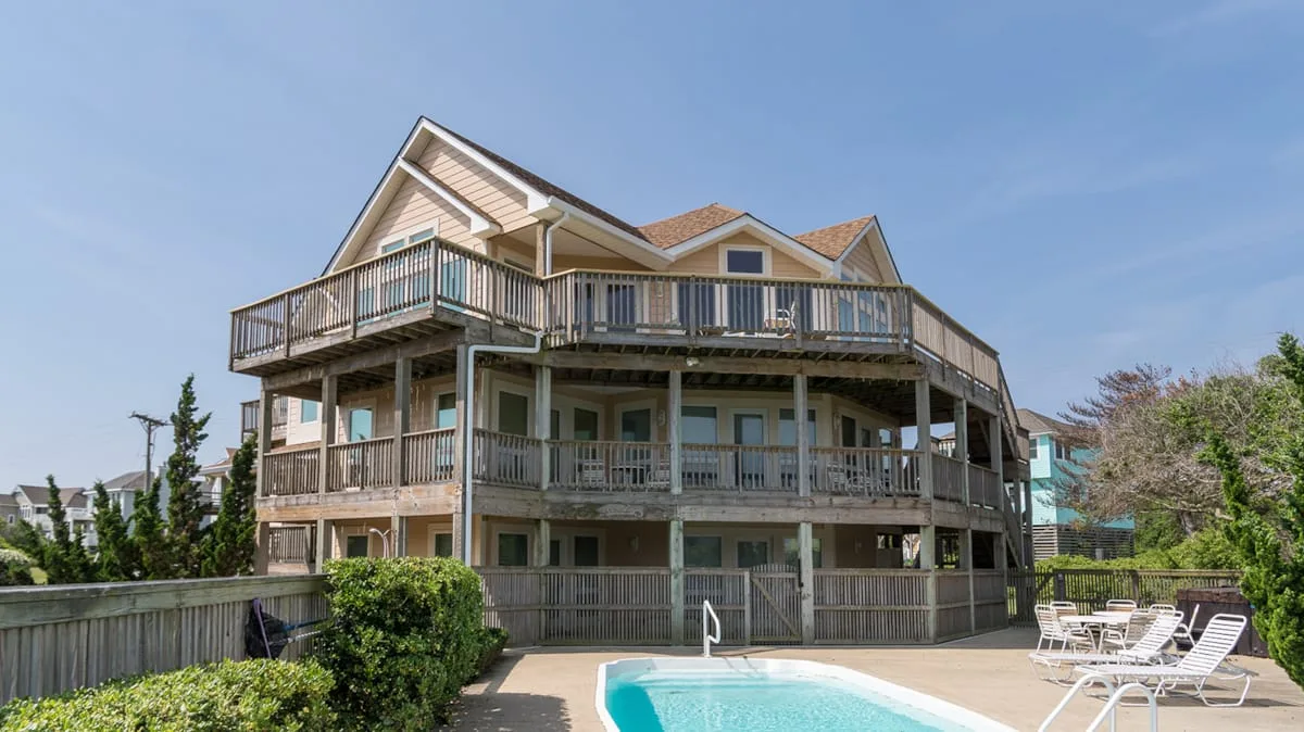 Una casa grande con terrazas envolventes se encuentra junto a una piscina al aire libre.