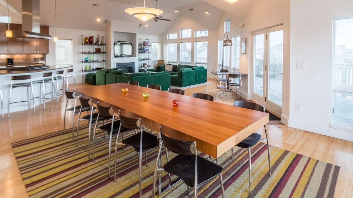 Un espacio abierto de comedor y sala con una mesa larga de madera y asientos verdes.