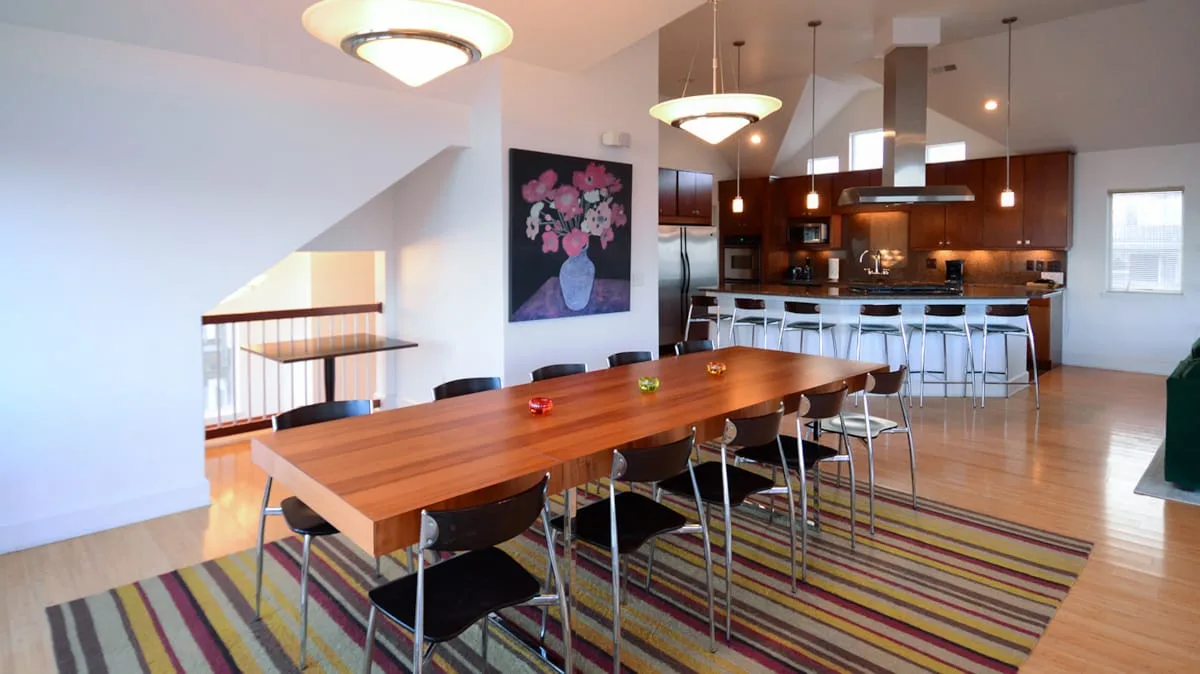 Comedor abierto con una mesa larga de madera y la cocina al fondo.
