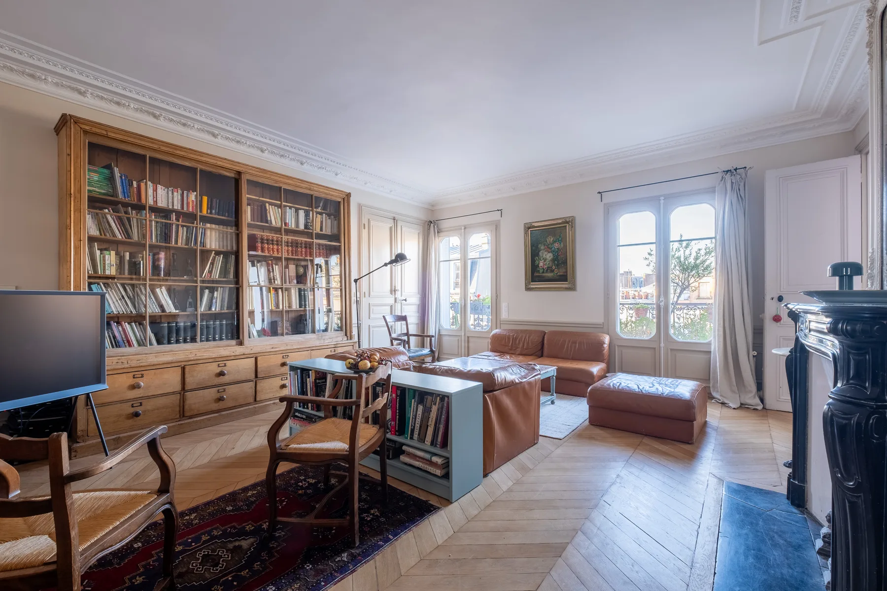 A bright living room with a large bookcase, seating, and tall windows.