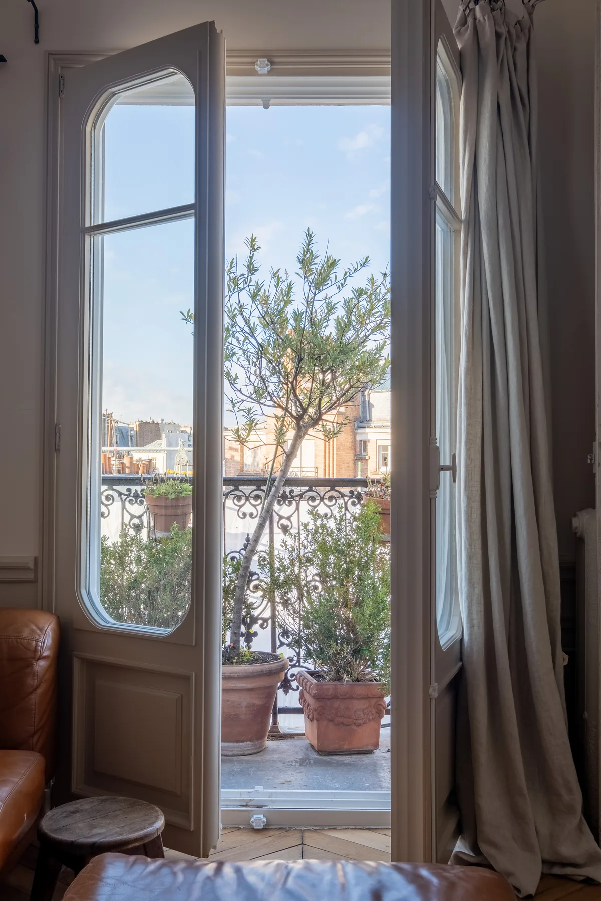 An open balcony doorway frames potted plants and a leafy tree.