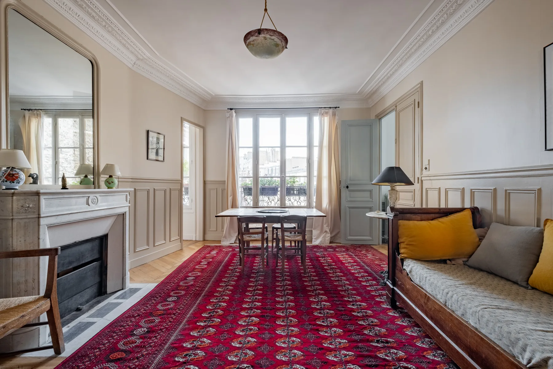 A bright sitting room with a fireplace, large windows, and a patterned rug.