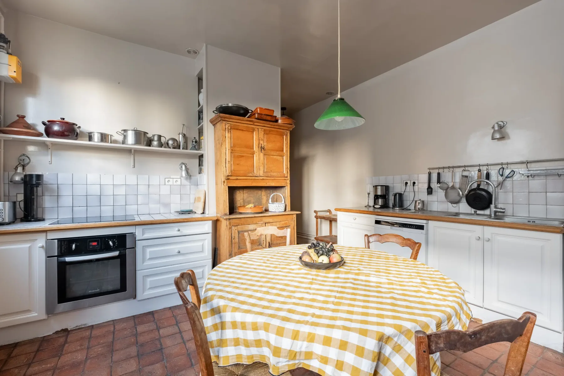 A kitchen and dining area with a round table covered in a yellow-and-white checked cloth.