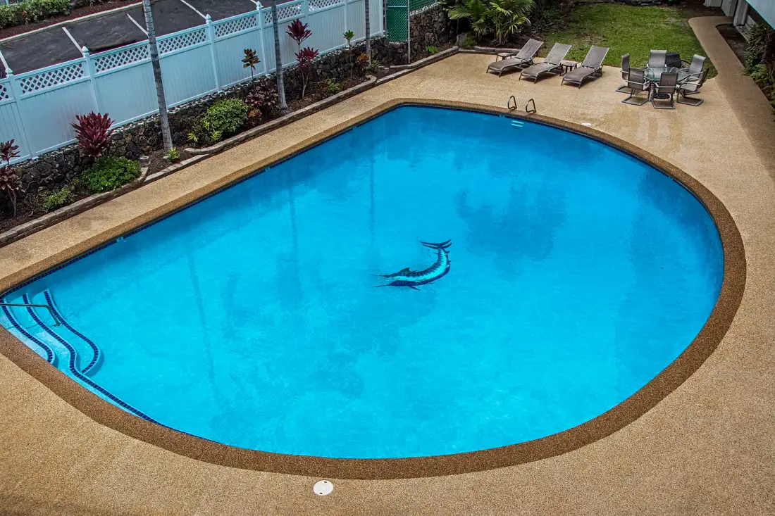 Una piscina al aire libre está rodeada por una terraza pavimentada y asientos de descanso.
