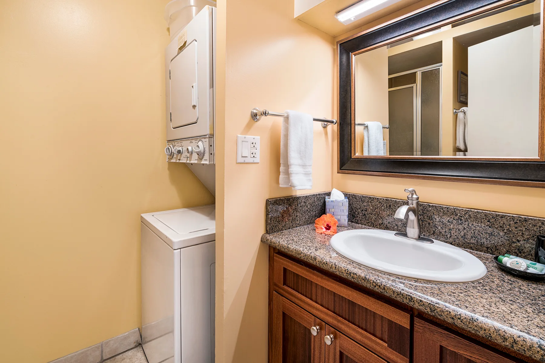 Un lavabo de baño con espejo junto a una lavadora y secadora apiladas.