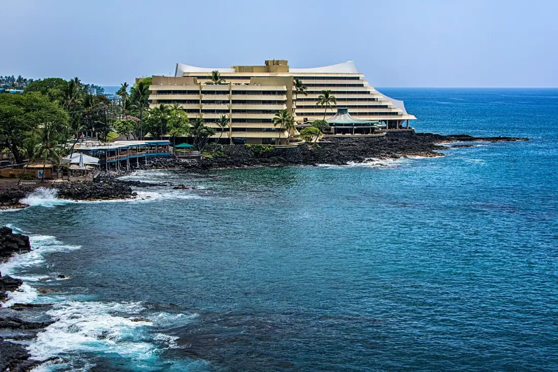 Un gran edificio frente al mar se encuentra junto a una costa rocosa y aguas azules.