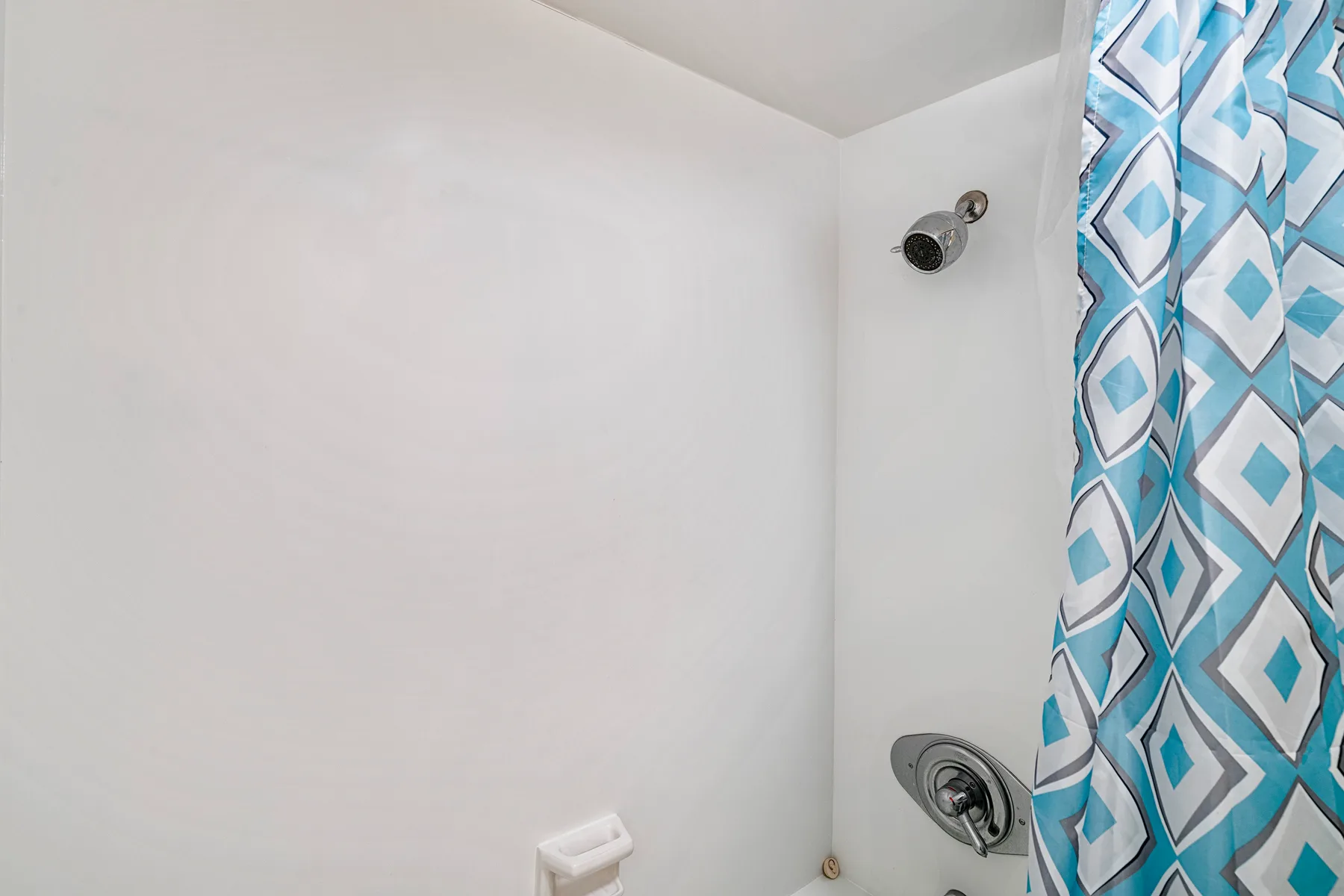 Zona de ducha de un baño con una cortina estampada azul y blanca.