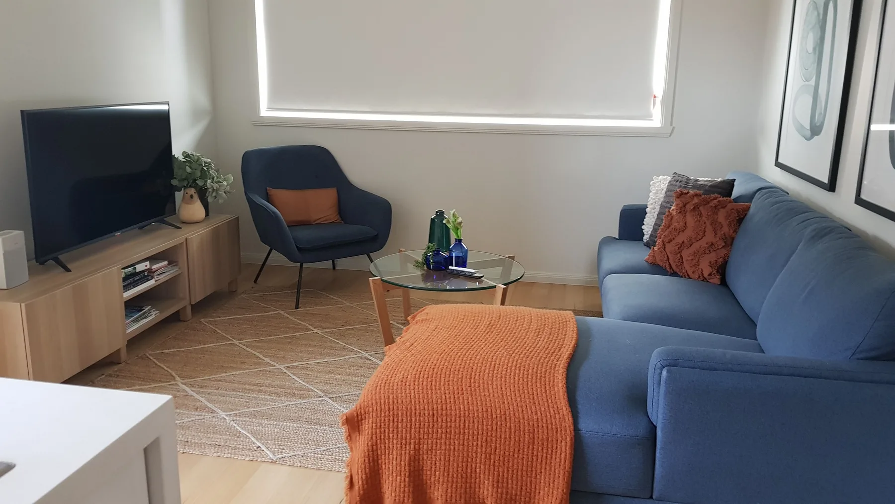 Una sala de estar con asientos azules, un televisor y una manta naranja.