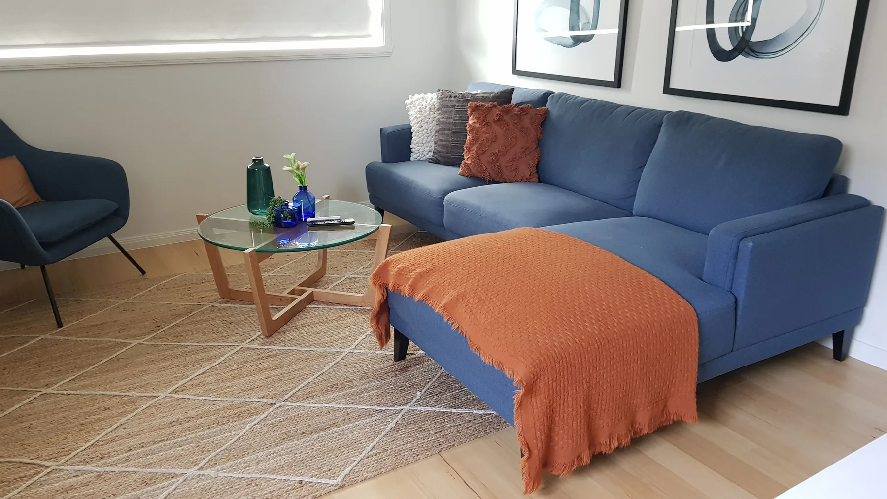 Sala de estar con asientos azules, una mesa de centro de vidrio y cuadros enmarcados.