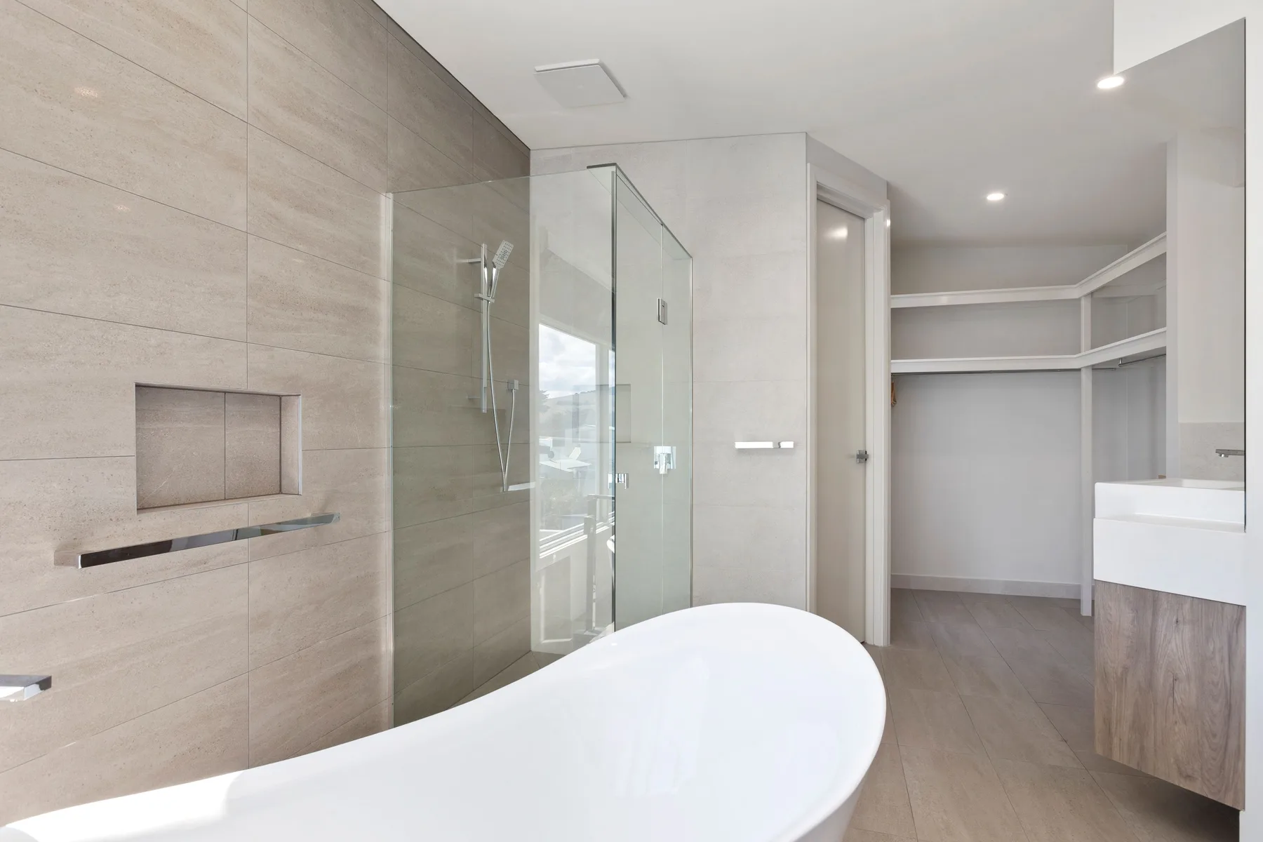 Un baño moderno cuenta con una bañera, una ducha de vidrio y estantes abiertos.