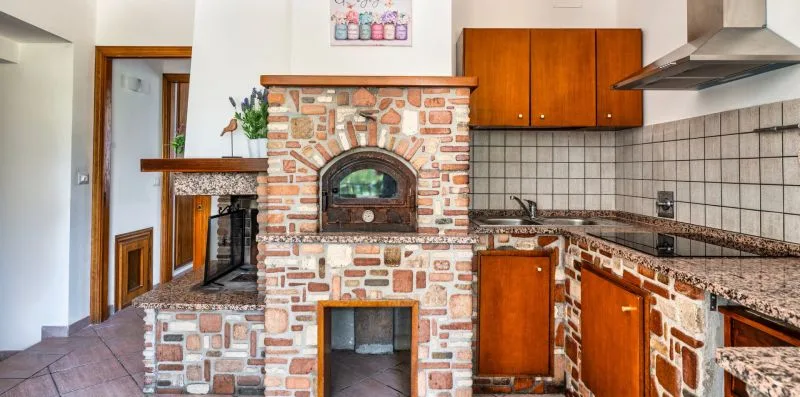 A kitchen with wood cabinets, tiled counters, and a brick cooking area.