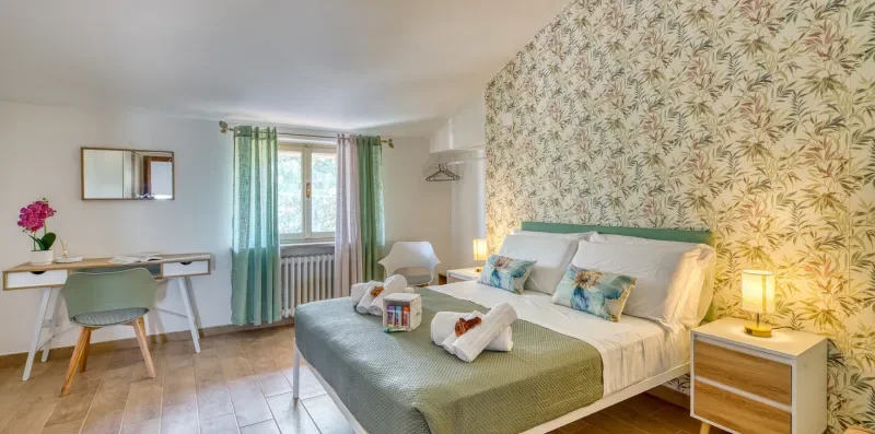 A bedroom with a bed, patterned wallpaper, and a small desk by the window.