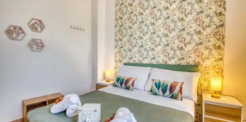 A bedroom with a neatly made bed against a patterned wall.