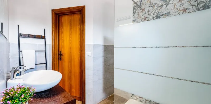 A bathroom with a sink, wooden door, and tiled shower area.