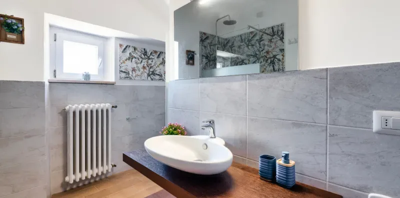 A bathroom with a wall-mounted sink, radiator, and glass shower screen.