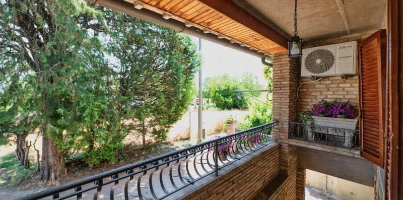 A covered balcony overlooks leafy greenery, with a metal railing along its edge.
