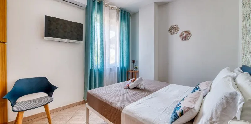 A bedroom with a bed, wall-mounted television, and teal curtains by the window.