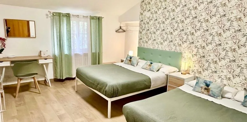 A bedroom with green bedding, a desk, and patterned wallpaper.