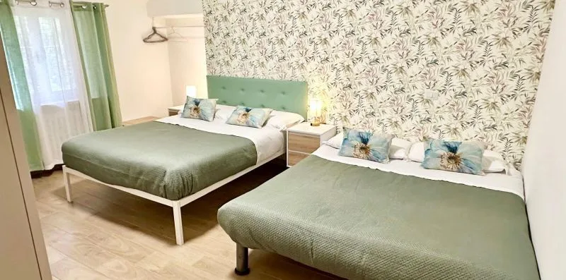 A bedroom with two beds, green bedding, and patterned wallpaper.