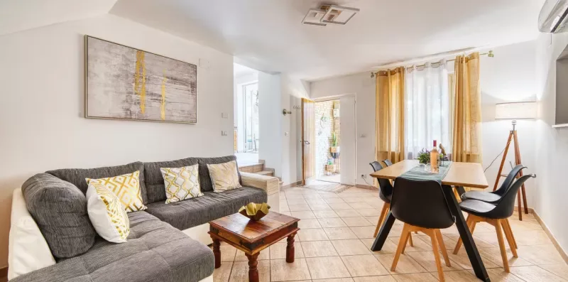 A bright living and dining area with gray seating and a table by the windows.