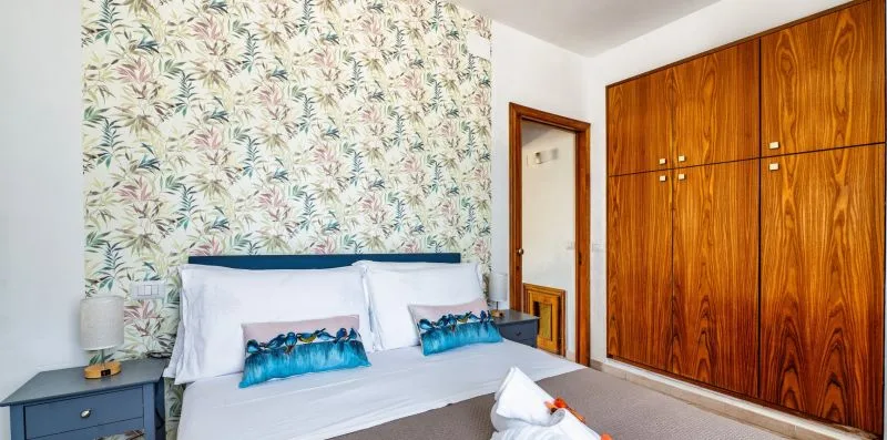 A bedroom with a bed, leafy wallpaper, and wooden wardrobes.