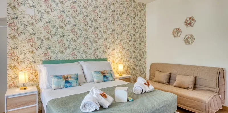 A bedroom with a bed, patterned wallpaper, and a sofa.