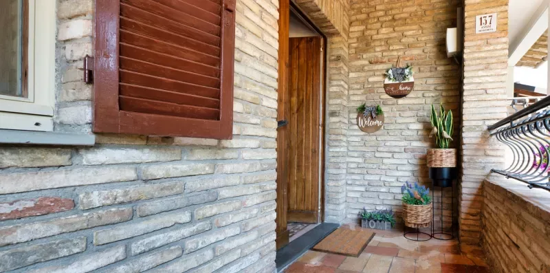 A brick entryway with a wooden door, potted plants, and a metal railing.