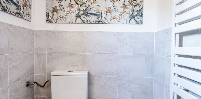 A bathroom with tiled walls, a toilet, and floral artwork above.