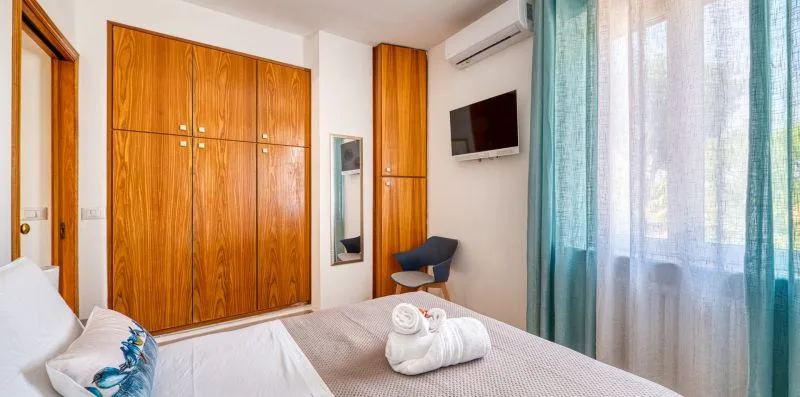 A bedroom with a bed, wooden wardrobes, and a curtained window.