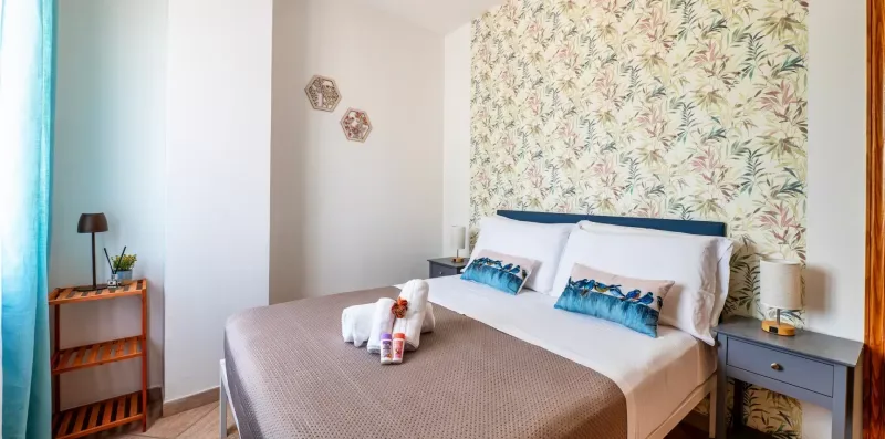 A bedroom with a neatly made bed and leafy patterned wallpaper.
