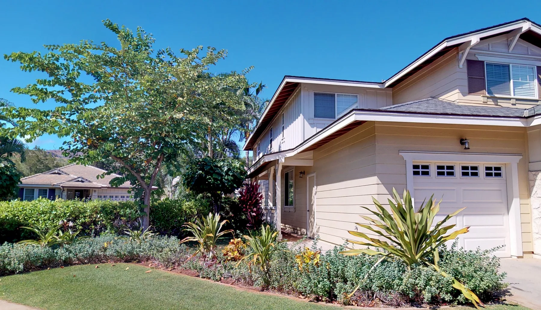Exterior de una casa suburbana con garaje, jardines y un árbol.