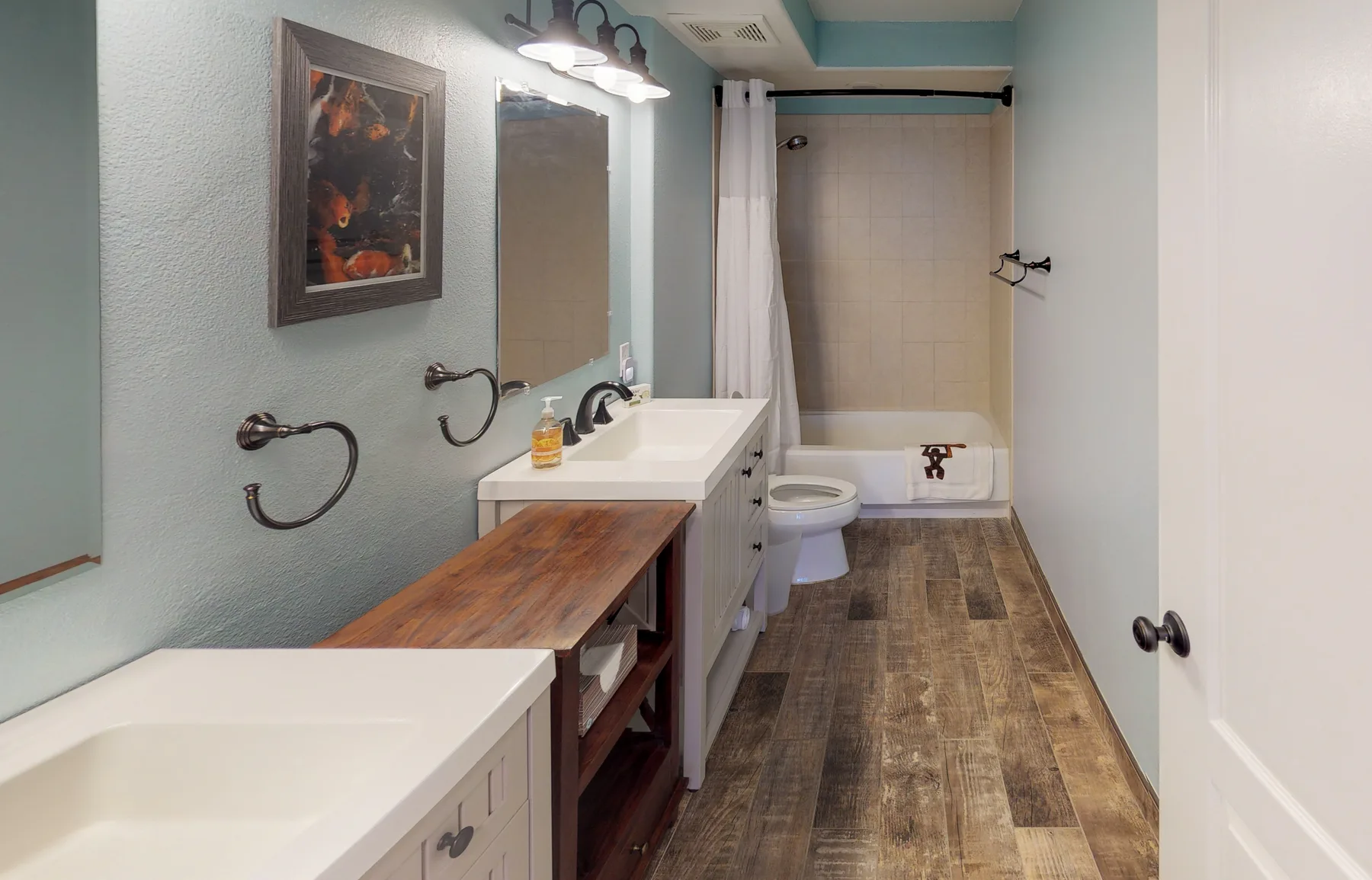 Un baño con un tocador largo, lavabos y una bañera detrás de una cortina de ducha.