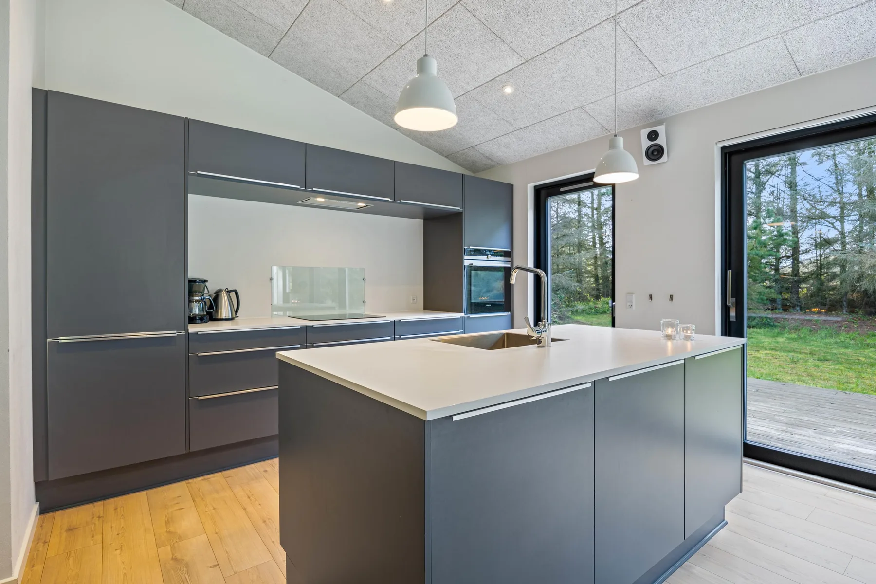 Una cocina moderna con gabinetes oscuros, una isla central y ventanas con vista a la vegetación.