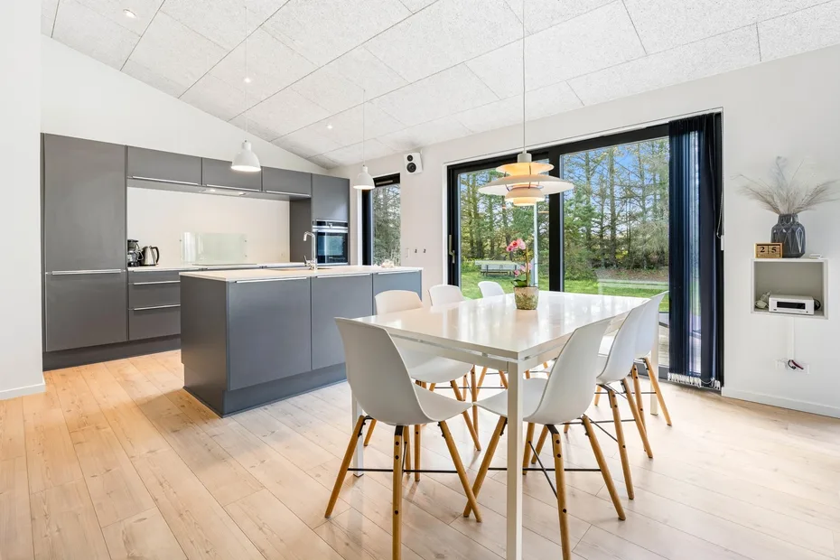 Una luminosa cocina-comedor de planta abierta con grandes ventanas que dan a la vegetación.