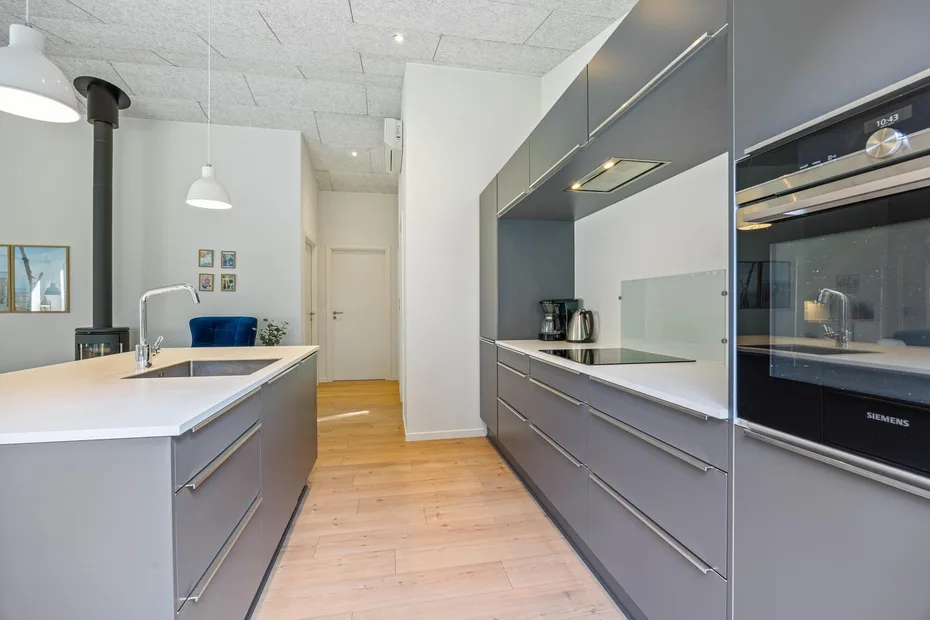 Una cocina moderna con gabinetes grises, una isla central y electrodomésticos integrados.