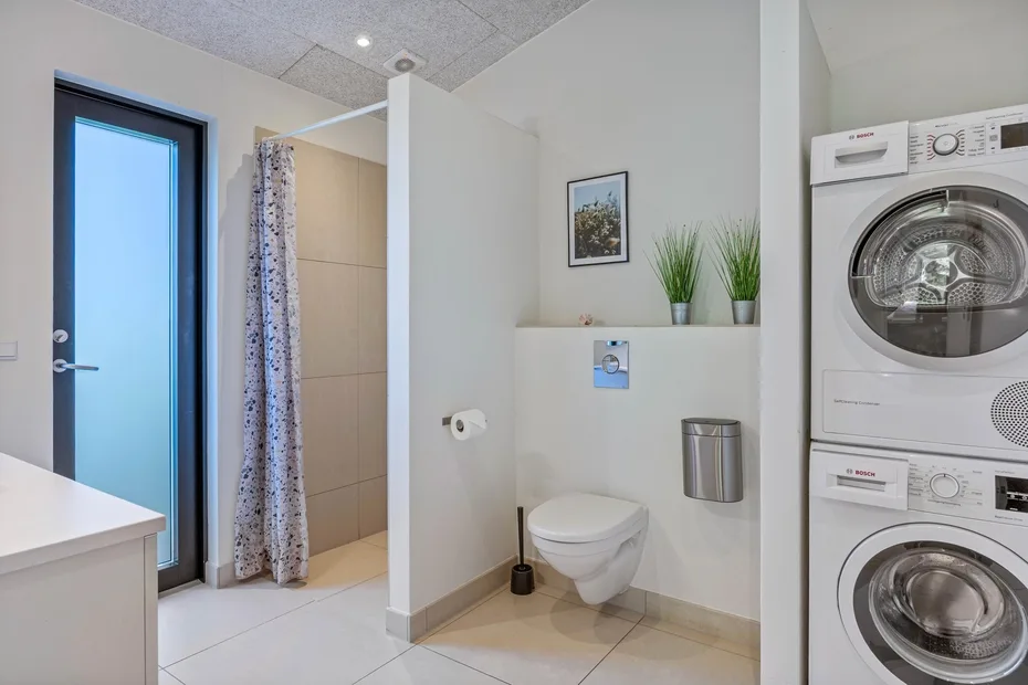 Un baño luminoso con ducha, inodoro y lavadoras apiladas.