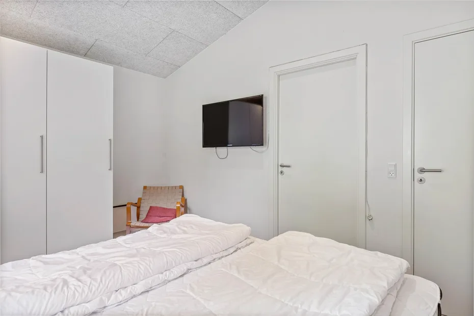 Un dormitorio con dos camas, un armario y un televisor montado en la pared.