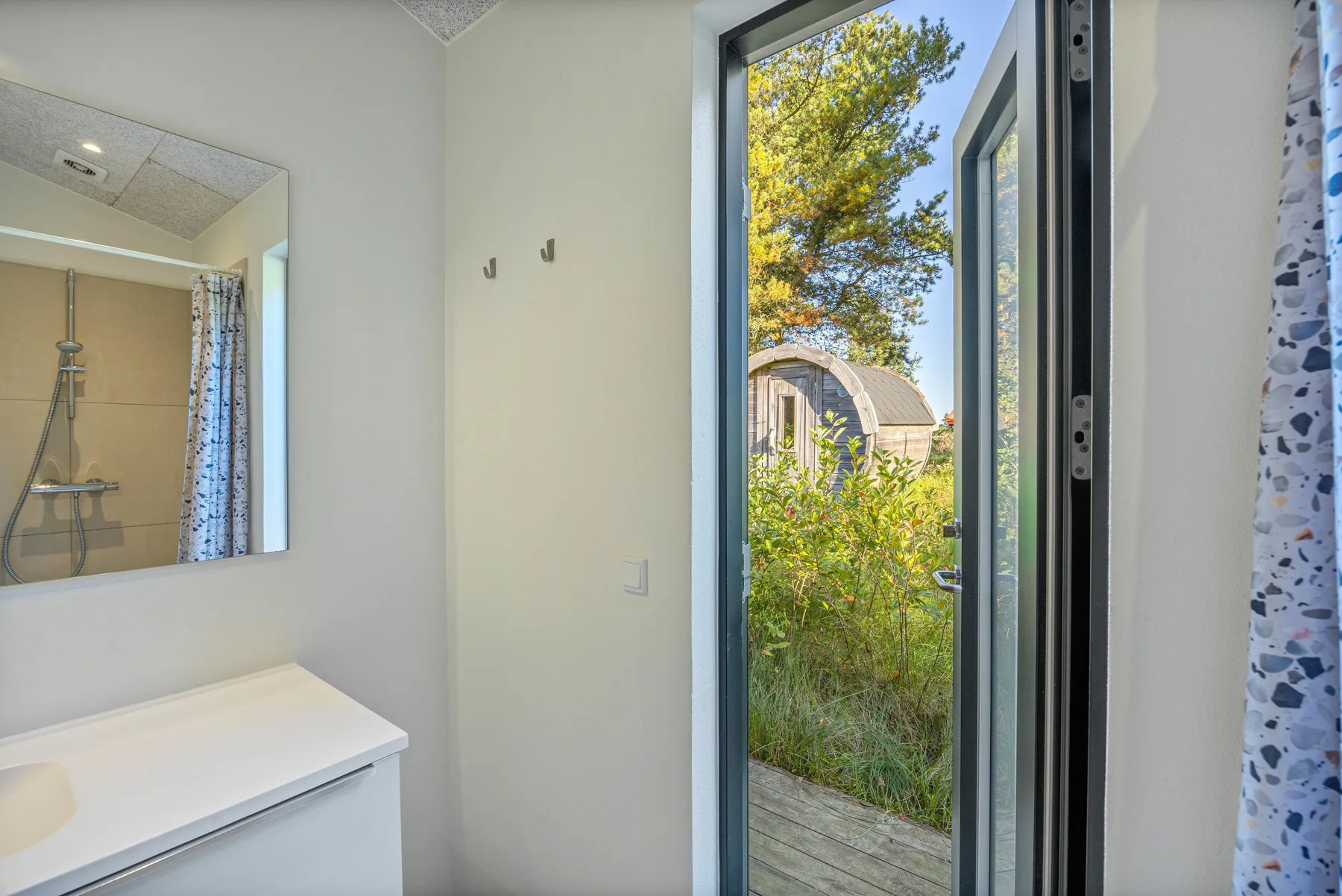 Un baño con lavabo y una puerta abierta que da a una zona verde.