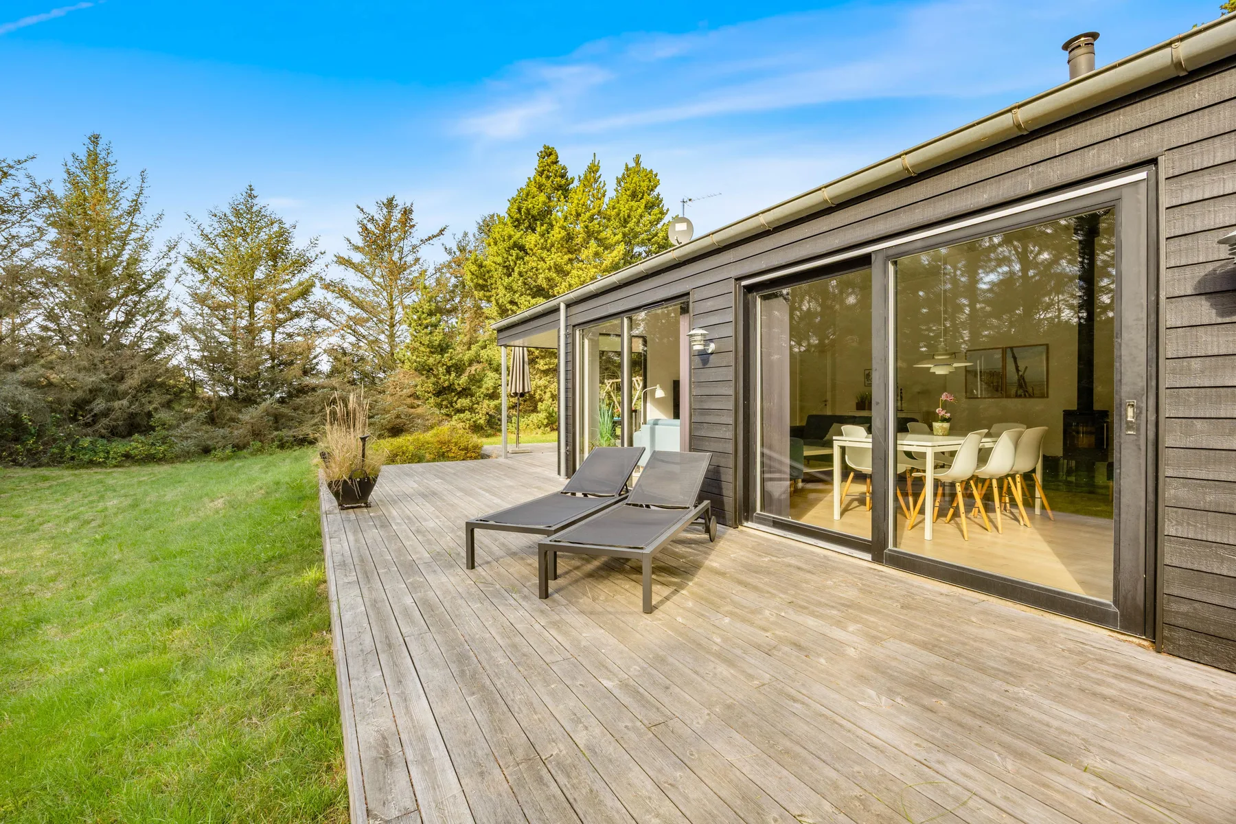 Una terraza de madera junto a una casa moderna da a un jardín con césped.
