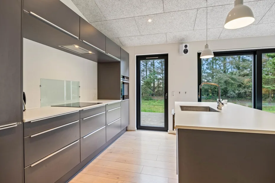 Una cocina moderna con gabinetes oscuros, una isla central y grandes ventanas.