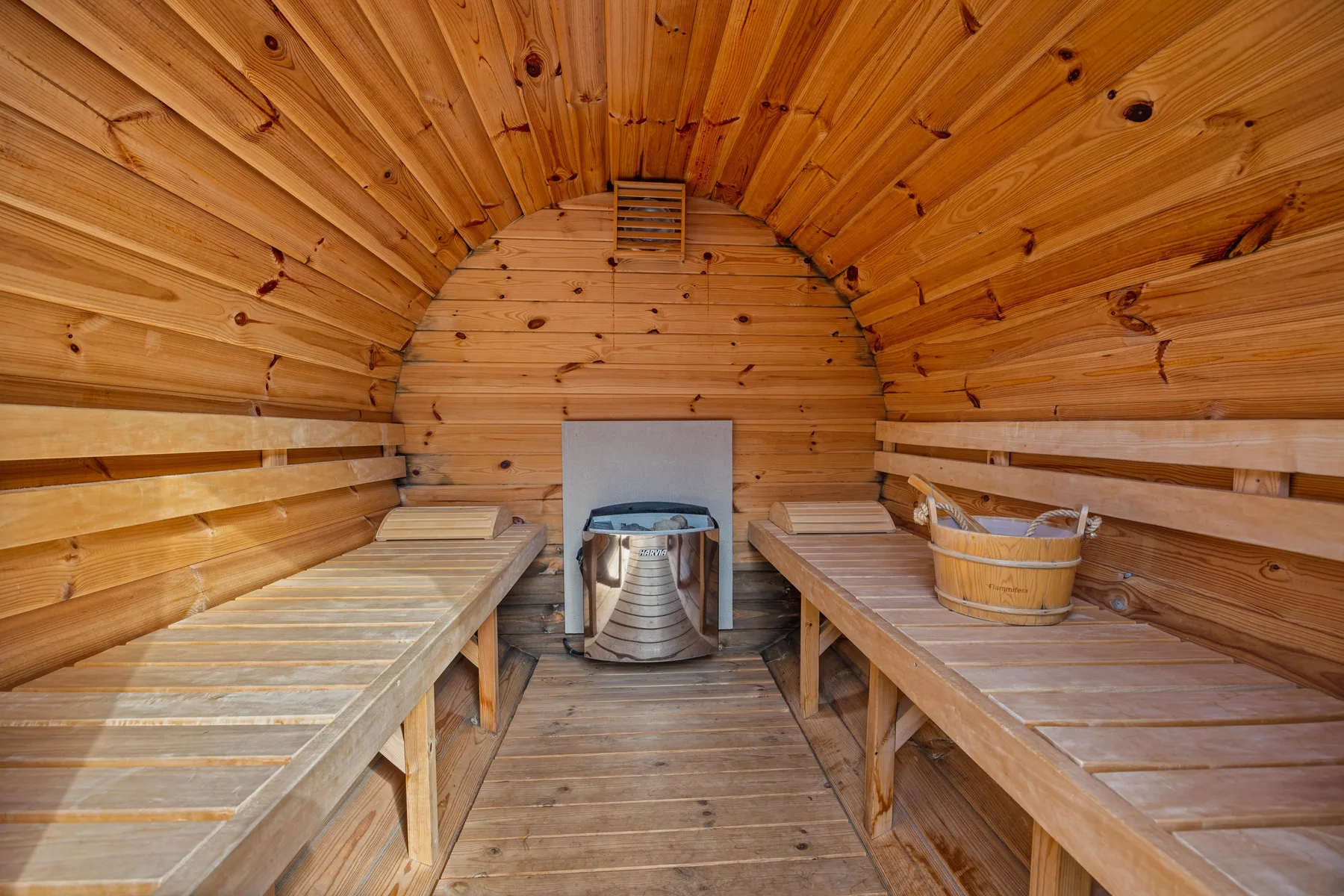 Interior de sauna de madera con bancos escalonados y un calentador al fondo.