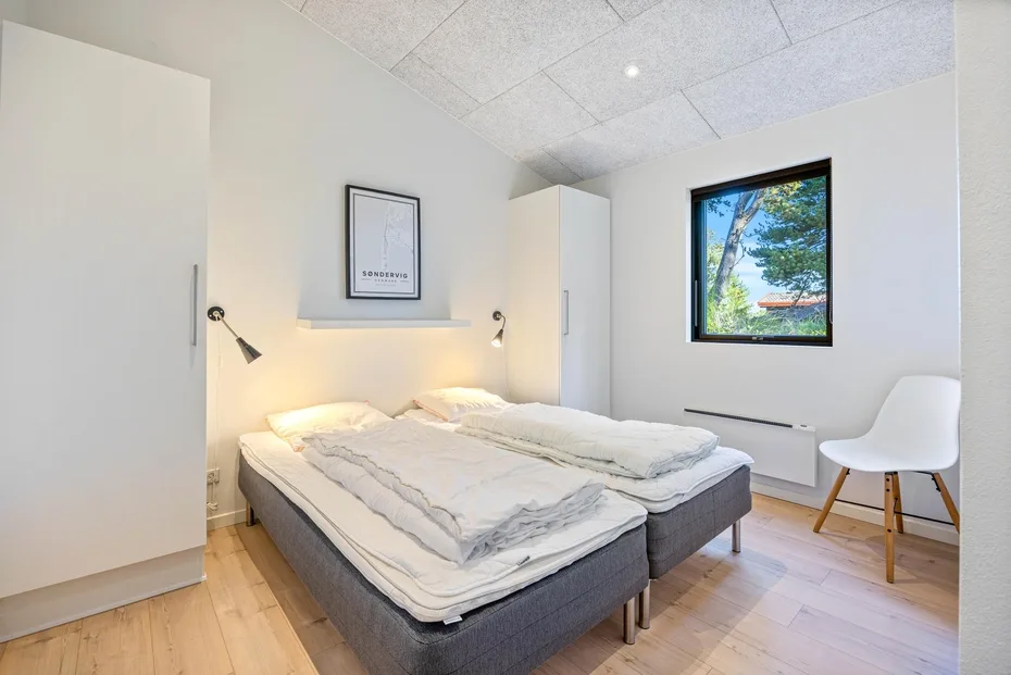 Un dormitorio luminoso con una cama doble y una ventana con vistas a los árboles.